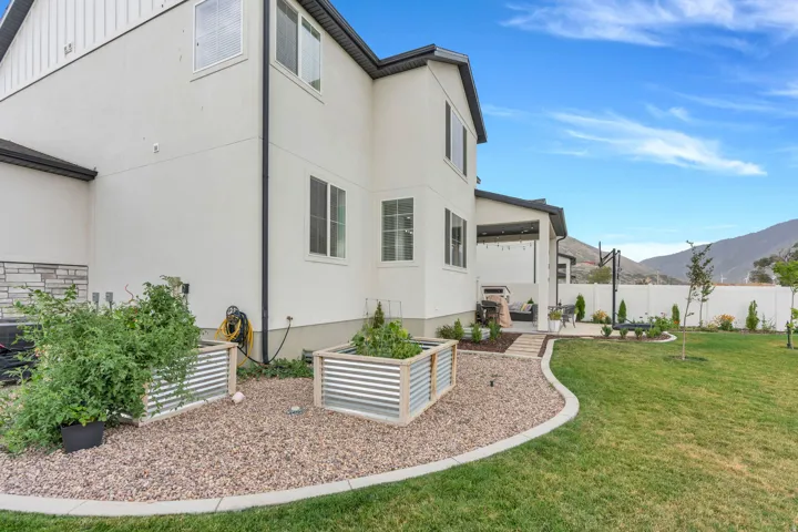 Exterior featuring a covered patio, paved walkway, manicured lawn, and raised garden beds