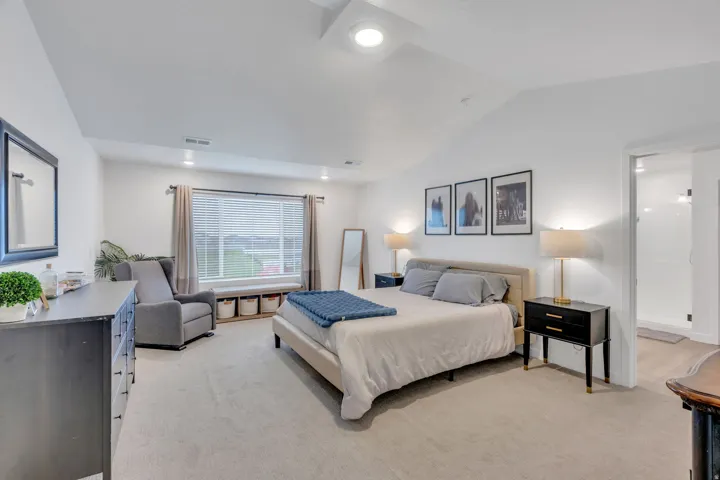 Vaulted ceiling, recessed lighting, carpet flooring, large window with blinds, and an open doorway