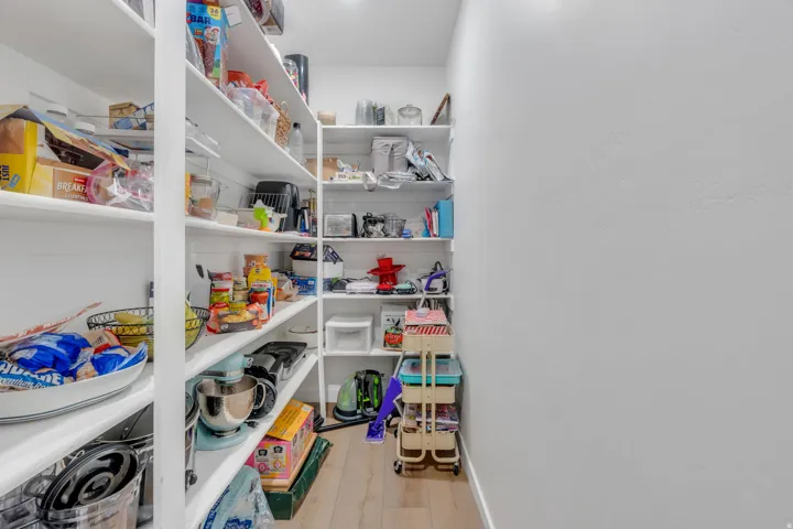 Walk-in pantry featuring extensive built-in shelving, white painted walls, and wood-finish flooring