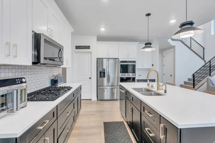 Kitchen with white upper cabinetry and dark lower cabinetry, stainless steel appliances, a tile backsplash, and light wood-finish flooring