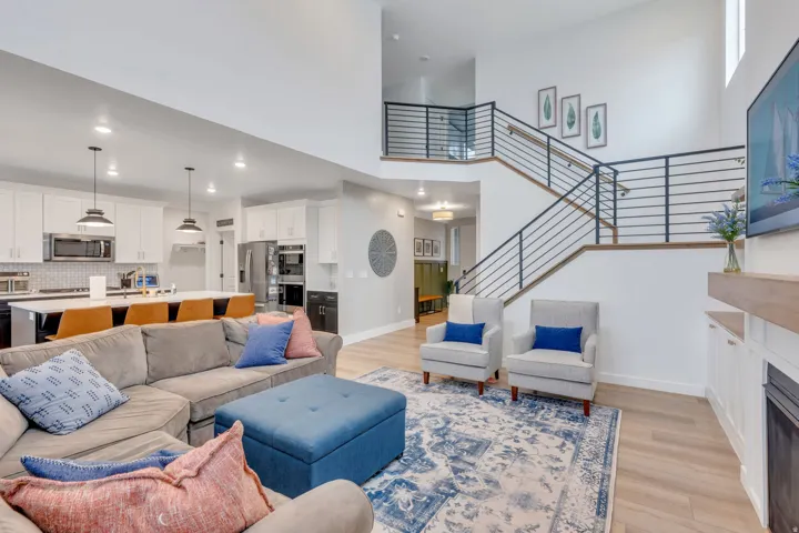 Open-concept living space with high ceilings, wood-finish flooring, and a modern staircase featuring horizontal iron railings