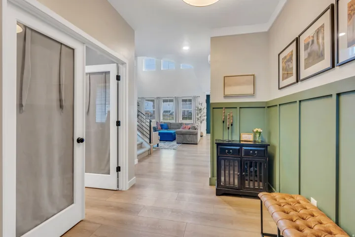 Light wood-finish flooring, half-wall board and batten paneling, recessed lighting, and a contemporary staircase with metal railings