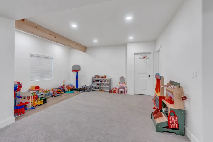 Spacious room featuring light gray carpeting, wood-finish flooring, a wood beam, recessed lighting, and a white window blind