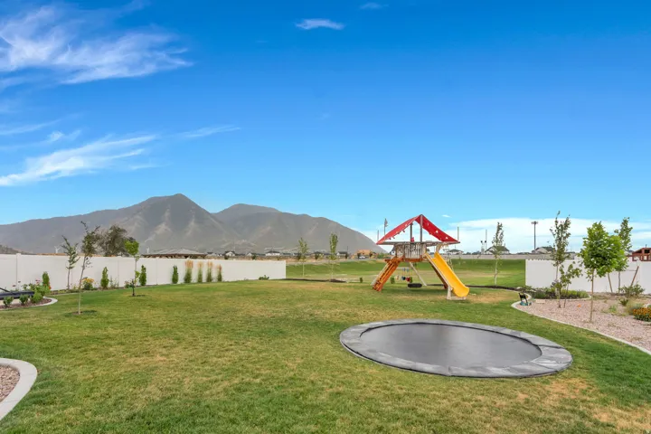Expansive lawn area with a white privacy fence, mountain backdrop, mature trees, and a landscaped perimeter