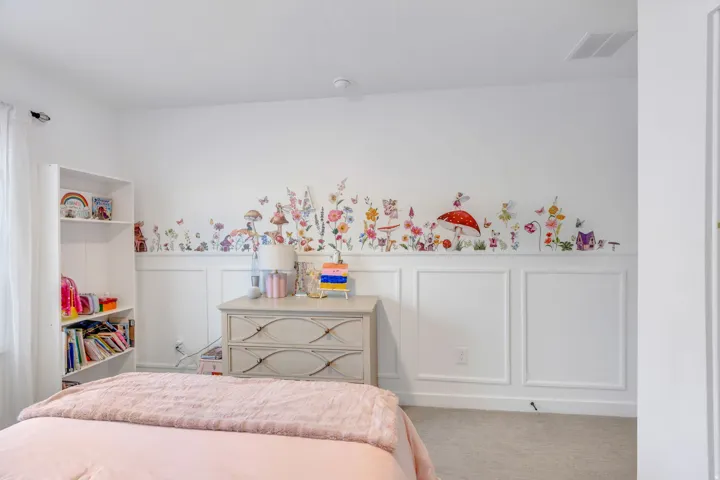 White paneled accent wall with decorative elements, light-toned carpeting, and a built-in shelving unit