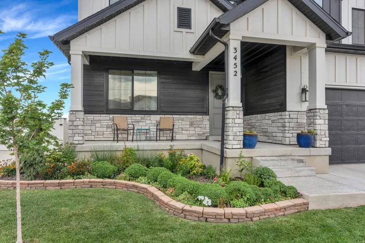 Contemporary exterior featuring white board and batten siding, dark horizontal siding, a stone facade, a covered front porch, and a landscaped front yard with a retaining wall