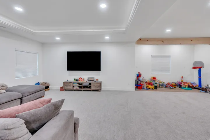 Recessed lighting illuminates a spacious room featuring crown molding, neutral-toned carpeting, and a wood beam accent