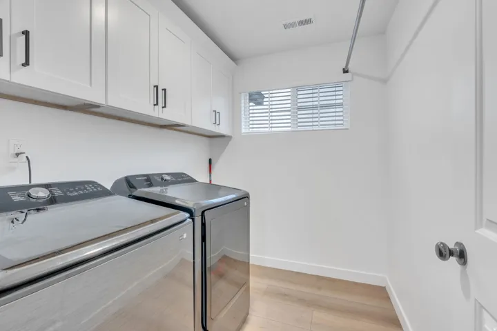 Laundry area featuring white shaker cabinetry, wood-finish flooring, a window with blinds, and white walls