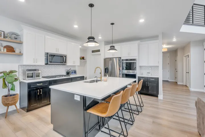 Kitchen featuring a large island with white countertop, two-tone cabinetry, tiled backsplash, stainless steel appliances, and wood-finish flooring