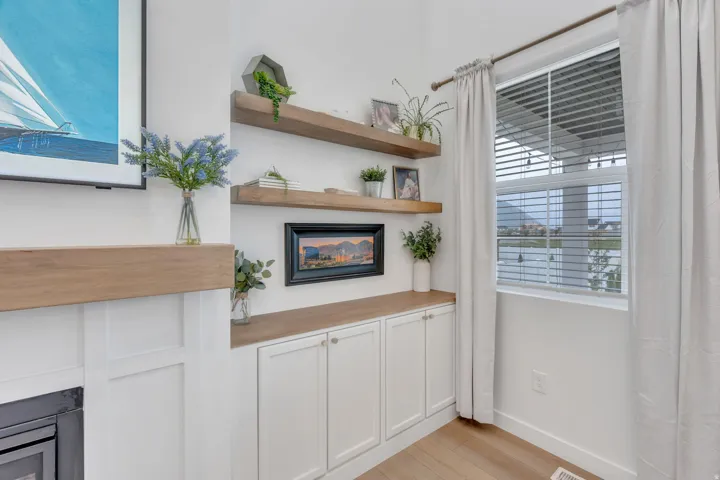 Fireplace with wood-finish mantel, built-in cabinetry with white shaker-style doors, wood-finish shelving, and a window with blinds