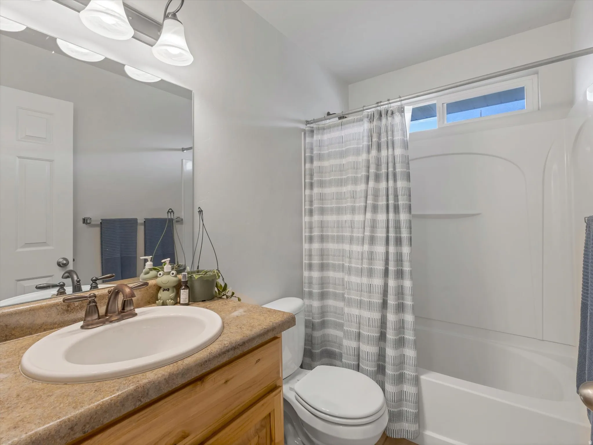 Bright bathroom featuring a wood-finish vanity with an undermount sink, natural stone countertop, and chrome faucet hardware