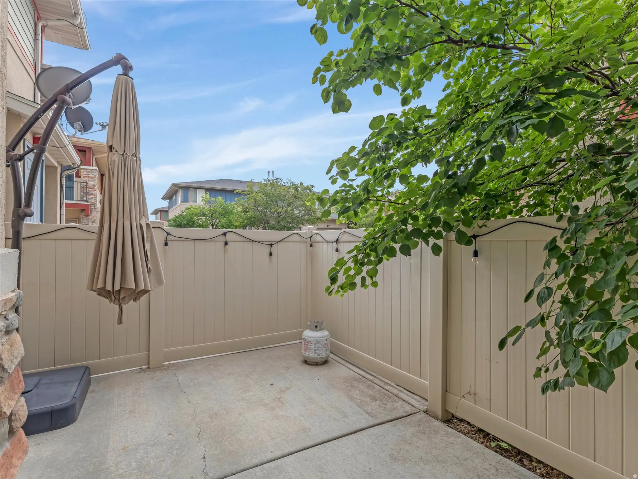 Private patio retreat enclosed by tall composite fencing, featuring a concrete surface, mature tree canopy overhead, and integrated outdoor lighting