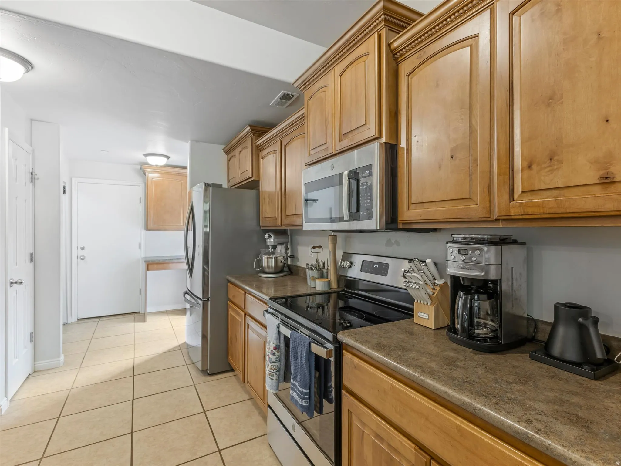 Kitchen featuring wood cabinetry, stainless steel appliances, durable countertops, and tile flooring