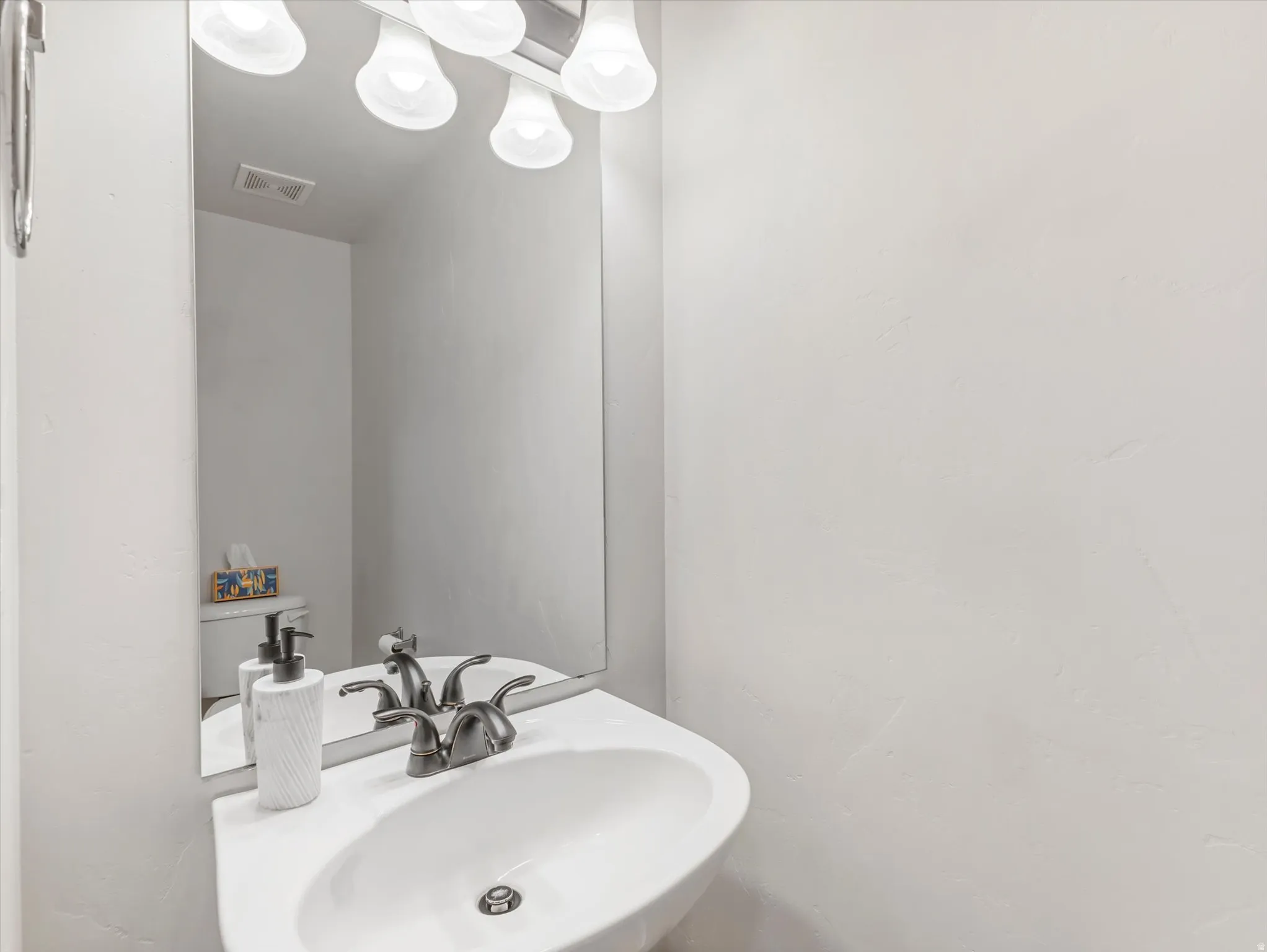 White pedestal sink with a dual-handle faucet, illuminated by a vanity light fixture