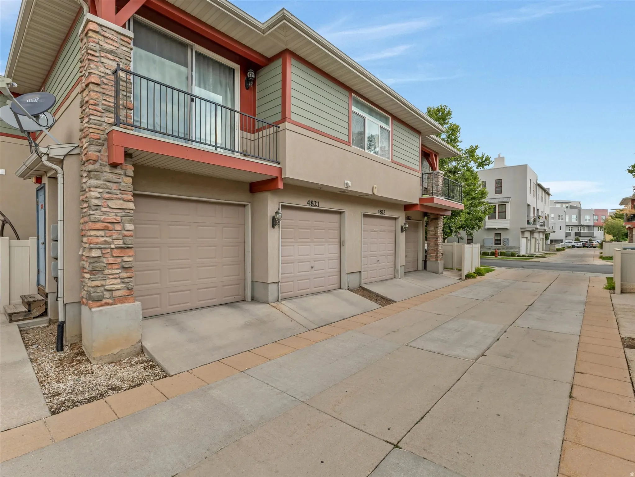Modern townhome featuring a three-car garage with individual bay doors, stone and siding exterior accents, and a wide concrete driveway with decorative brick paver borders
