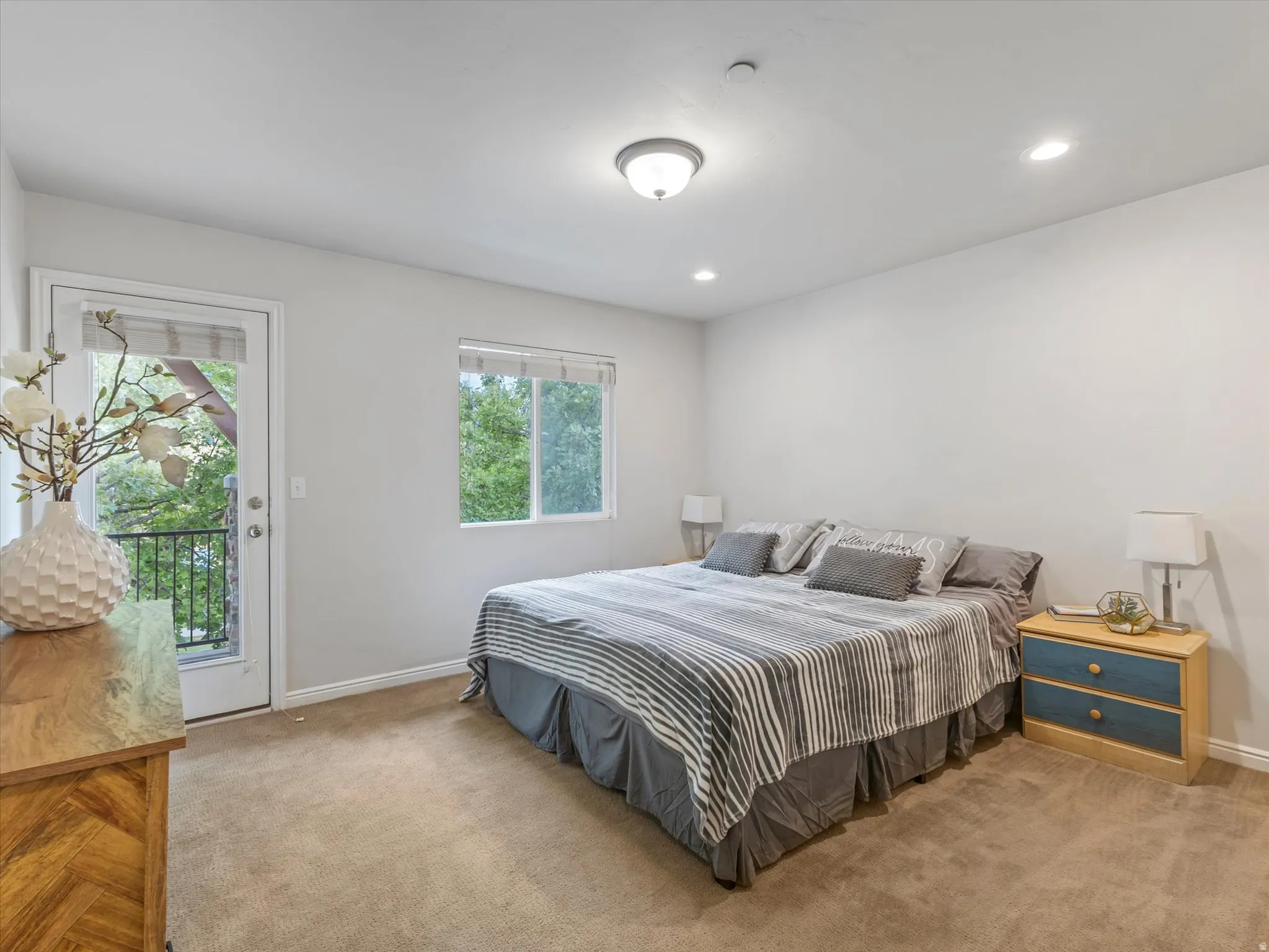 Spacious primary bedroom with carpeted flooring, recessed ceiling lighting, and dual windows and glass panel door leading to private balcony
