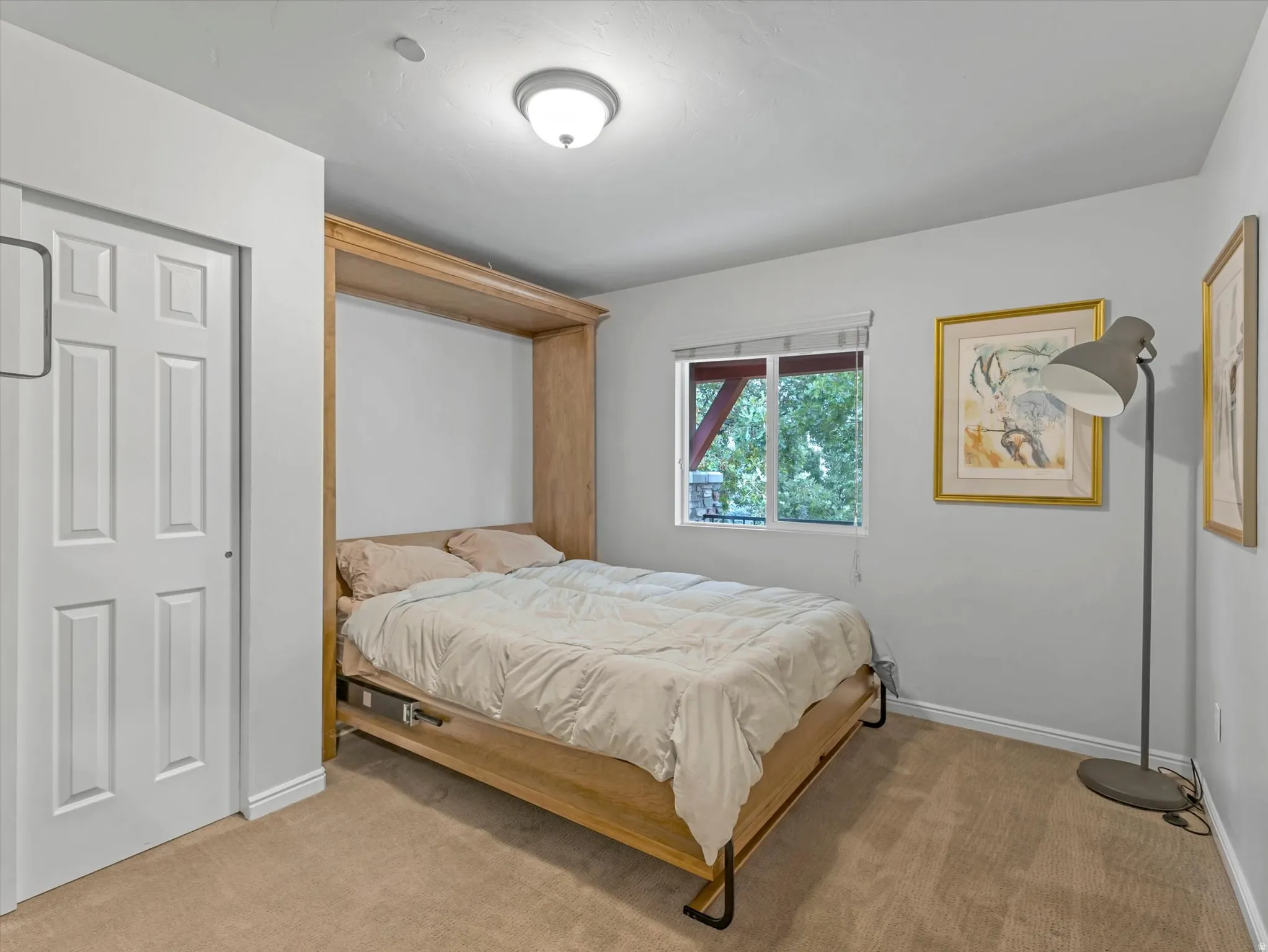 Recessed lighting, wood-toned Murphy bed, window with exterior foliage, white paneled door, and carpeted flooring