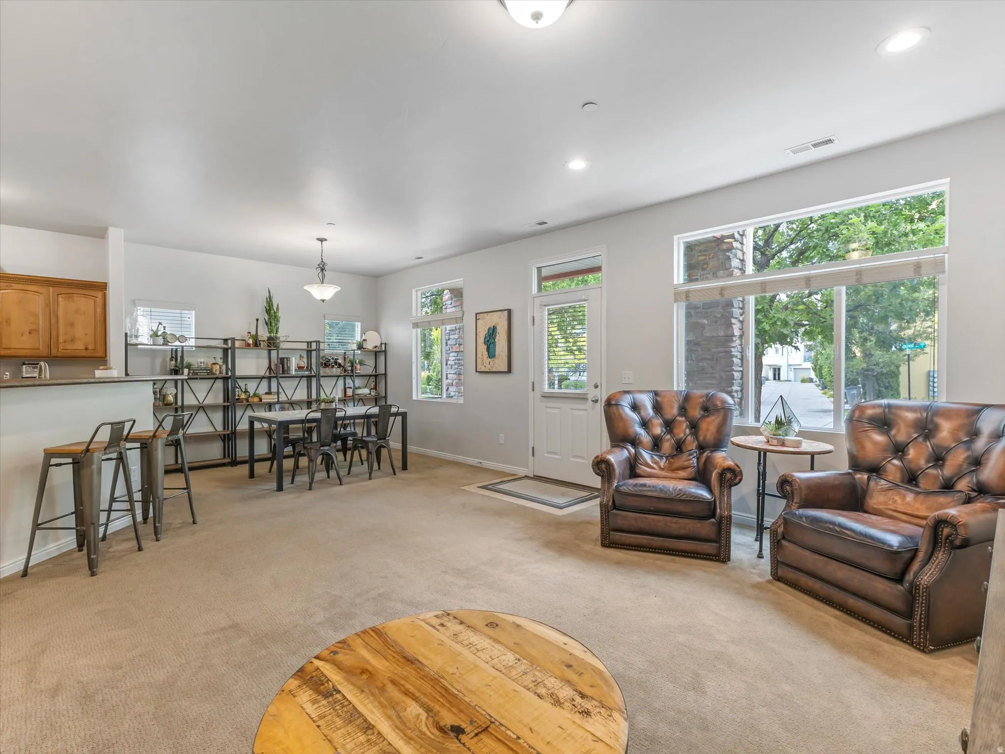 Open-concept living space featuring neutral carpeting, recessed ceiling lighting, and abundant natural light from expansive multi-pane windows and glass panel door
