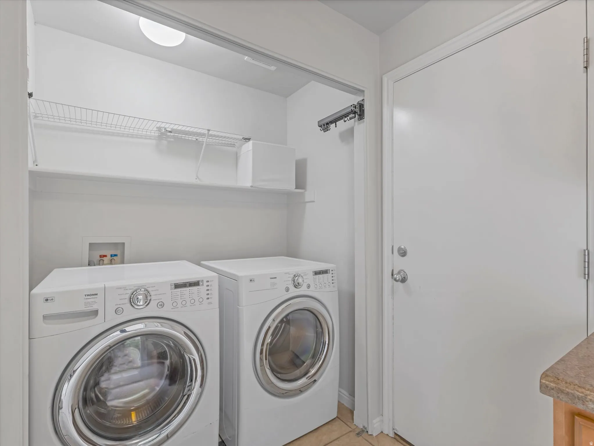 Laundry area featuring a ceiling light fixture, two white shelving units, and a tiled floor