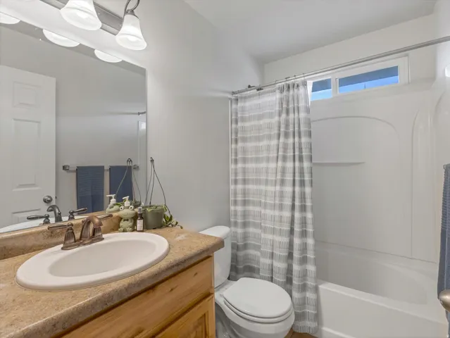 Bright bathroom featuring a wood-finish vanity with an undermount sink, natural stone countertop, and chrome faucet hardware