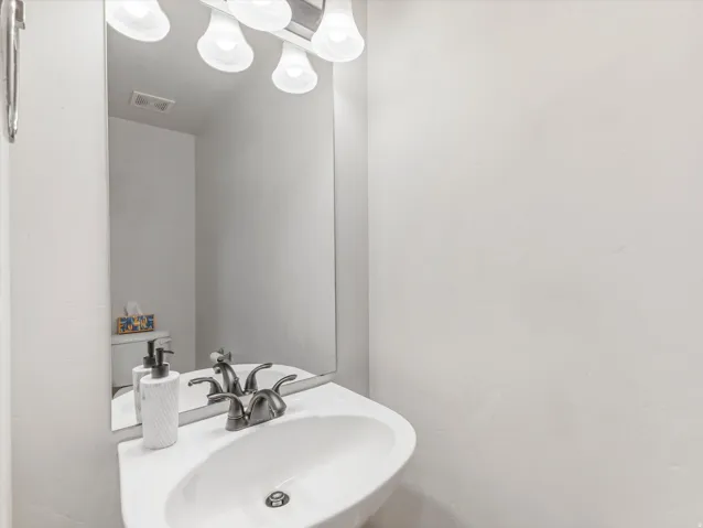White pedestal sink with a dual-handle faucet, illuminated by a vanity light fixture