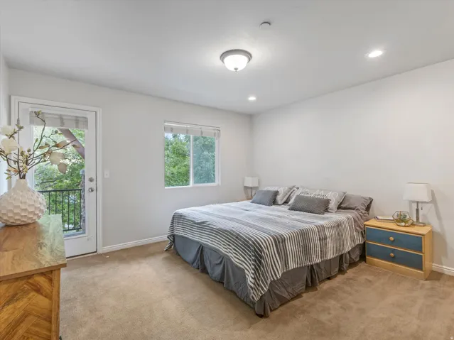 Spacious primary bedroom with carpeted flooring, recessed ceiling lighting, and dual windows and glass panel door leading to private balcony