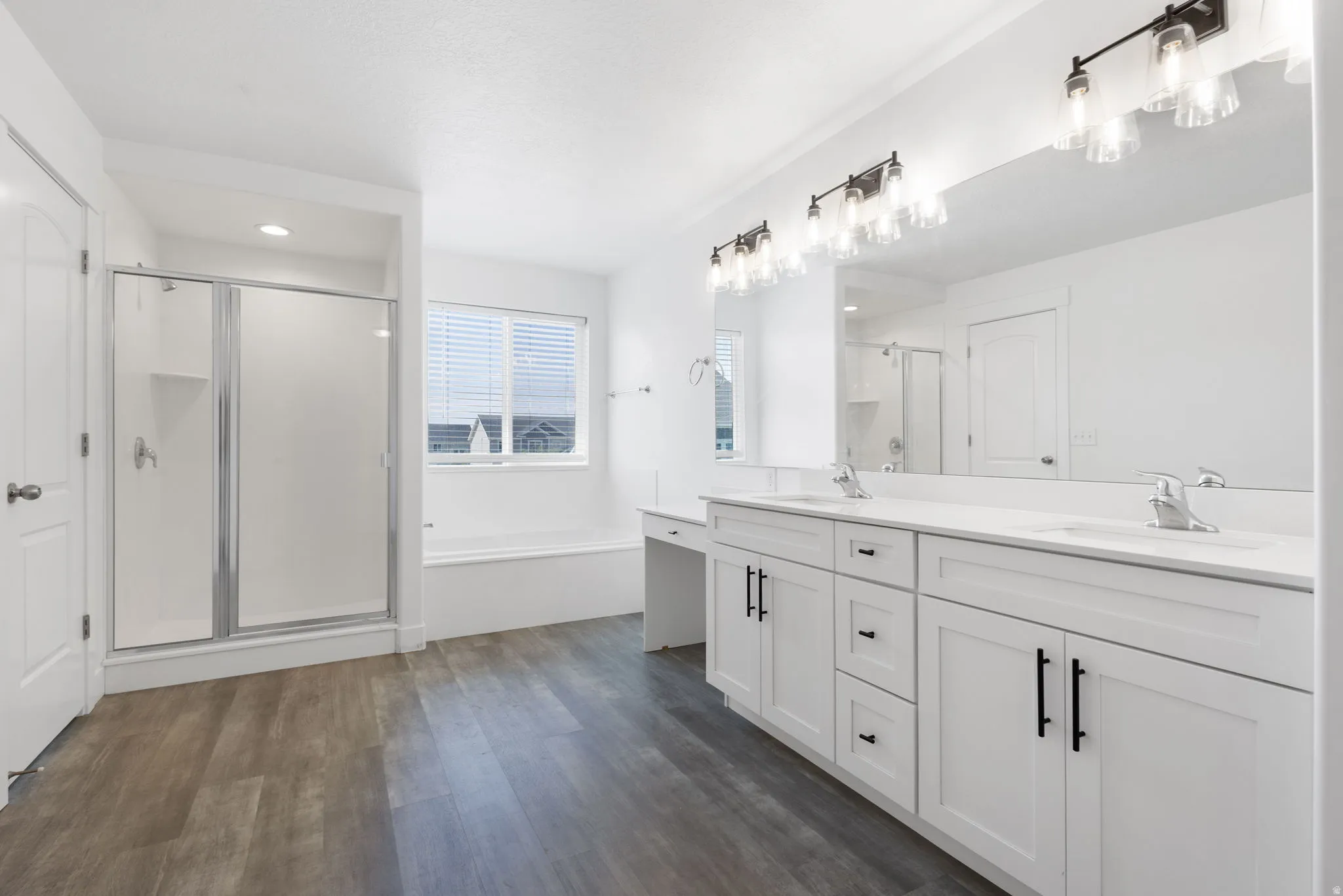 Primary bathroom with dual vanity with white cabinetry and black hardware, large mirror, recessed lighting, wood-finish flooring, and a walk-in shower with a glass enclosure