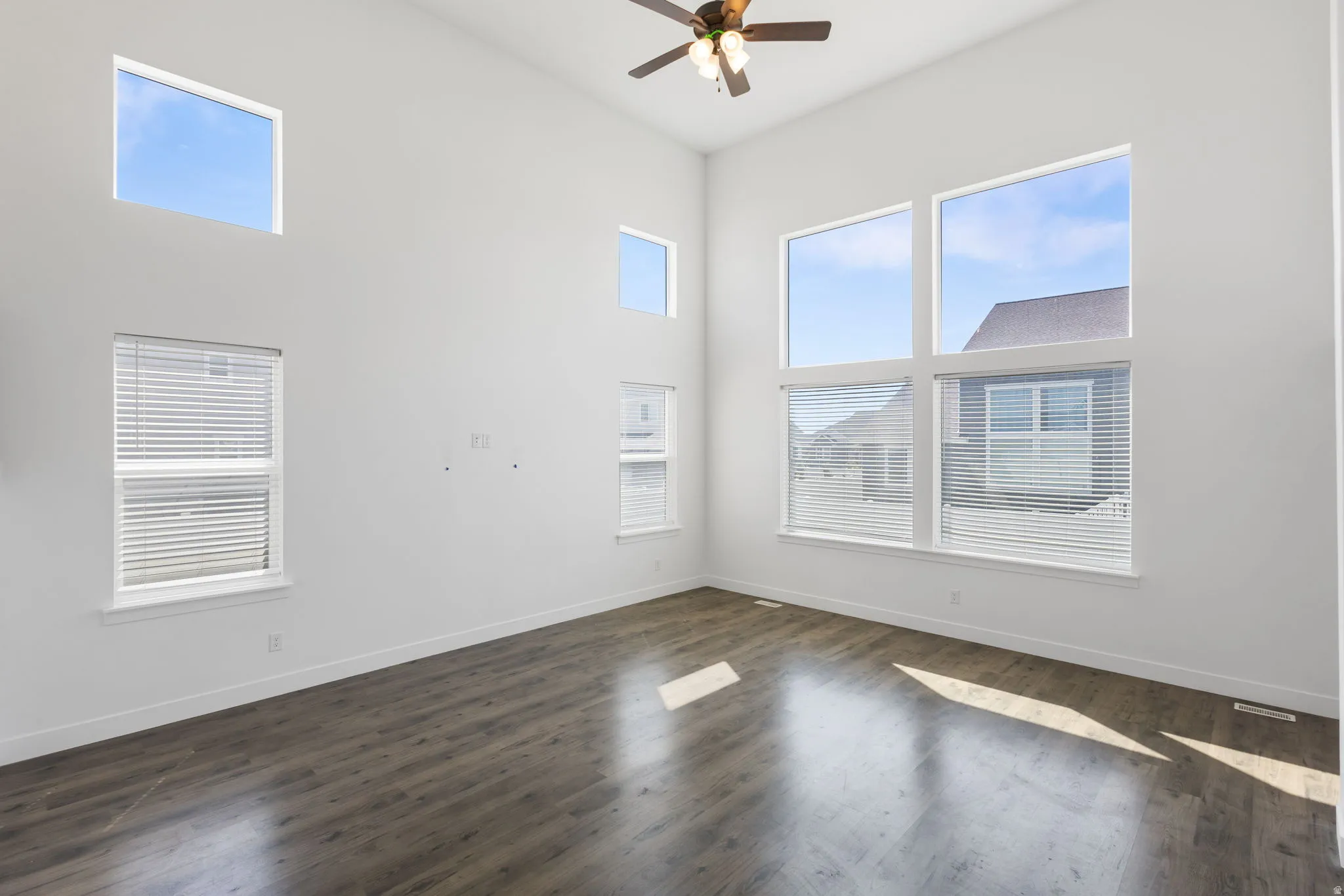 Vaulted ceiling featuring a ceiling fan, wood-finish flooring, and multiple large windows with blinds