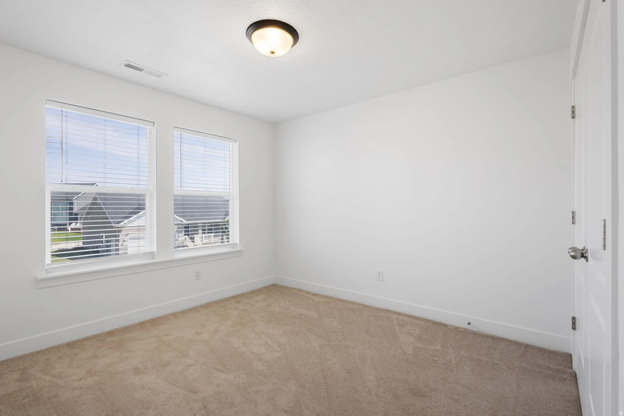 Bright, light-filled bedroom featuring dual windows with horizontal blinds, neutral wall finishes, and neutral-tone carpeting throughout