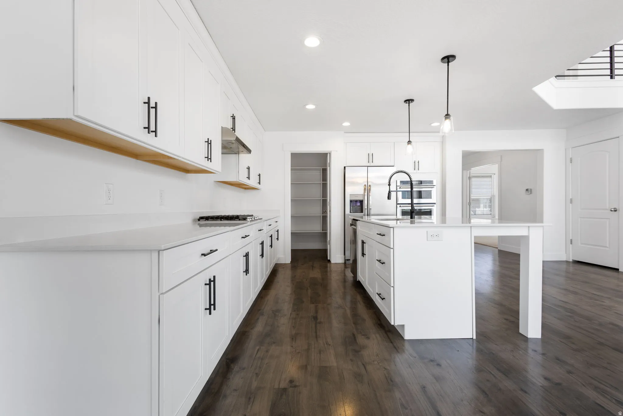 Modern kitchen featuring white cabinetry with hardware accents, wood-finish floating shelf, stainless steel appliances, subway tile backsplash, and dark wood-finish flooring throughout the open-concept space