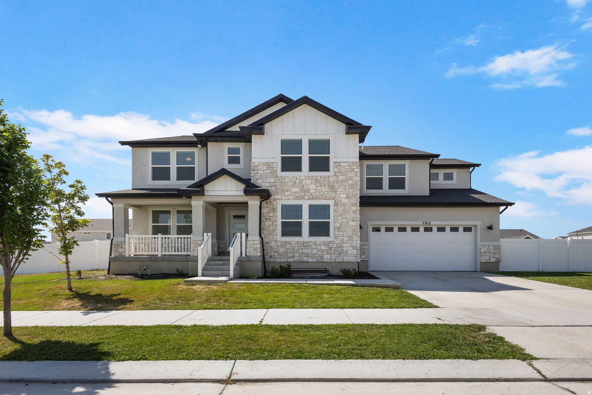 Two-story residence featuring a combination of stucco and stone veneer siding, a covered front porch, a two-car garage, and a concrete driveway