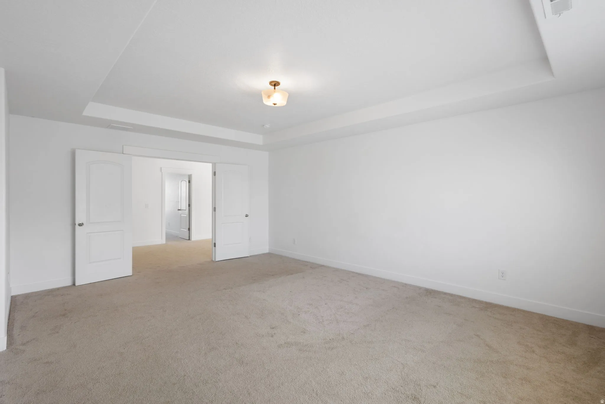Primary bedroom with spacious interior featuring neutral carpet flooring, white six-panel doors, a coffered ceiling with recessed lighting, and clean white walls throughout