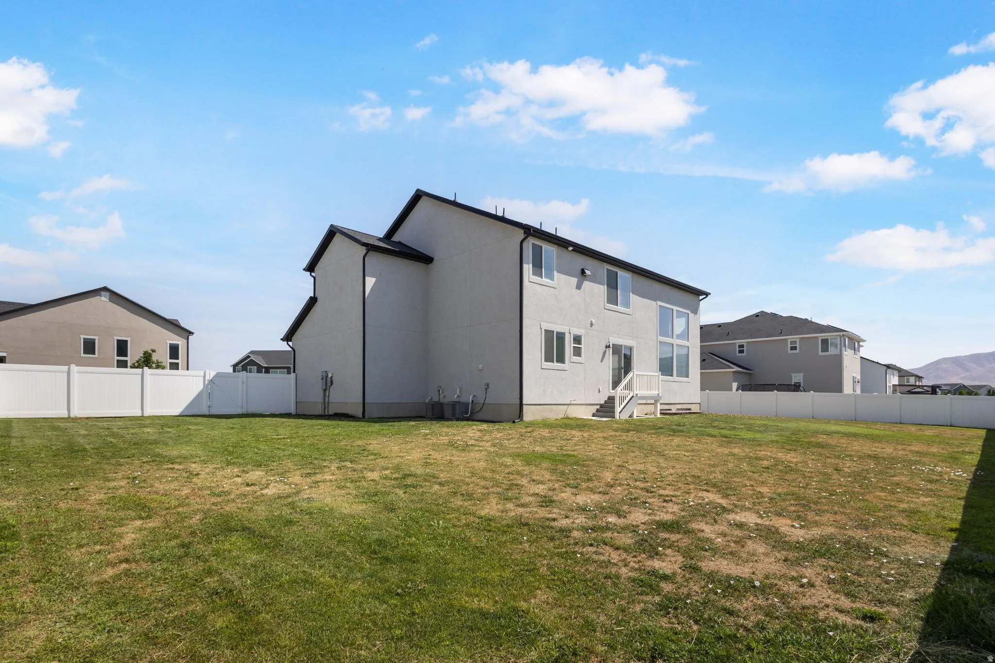 Expansive backyard featuring a stucco exterior, white vinyl fencing, and a multi-pane window design