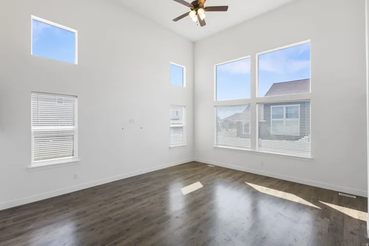 Vaulted ceiling featuring a ceiling fan, wood-finish flooring, and multiple large windows with blinds