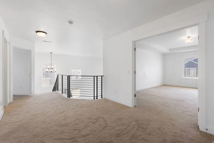 Spacious upper-level landing featuring wide-plank wood-finish flooring, abundant natural light from multiple windows, modern metal stair railing, and generous open layout with access to adjoining rooms