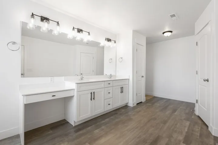 Primary bathroom with dual vanity with white cabinetry, integrated sinks, extended countertop, wood-finish flooring, and contemporary overhead lighting