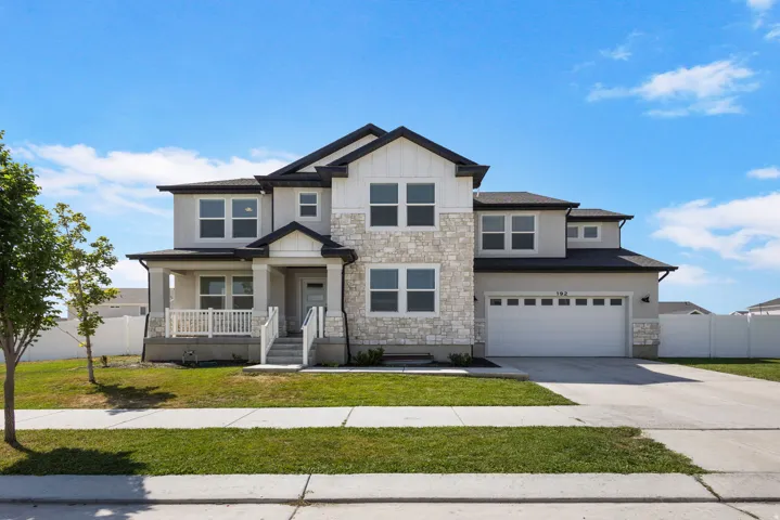 Two-story residence featuring a combination of stucco and stone veneer siding, a covered front porch, a two-car garage, and a concrete driveway