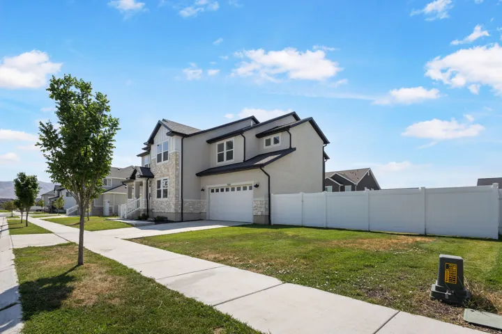 Two-story exterior with stone and stucco accents, a two-car garage, and a white privacy fence