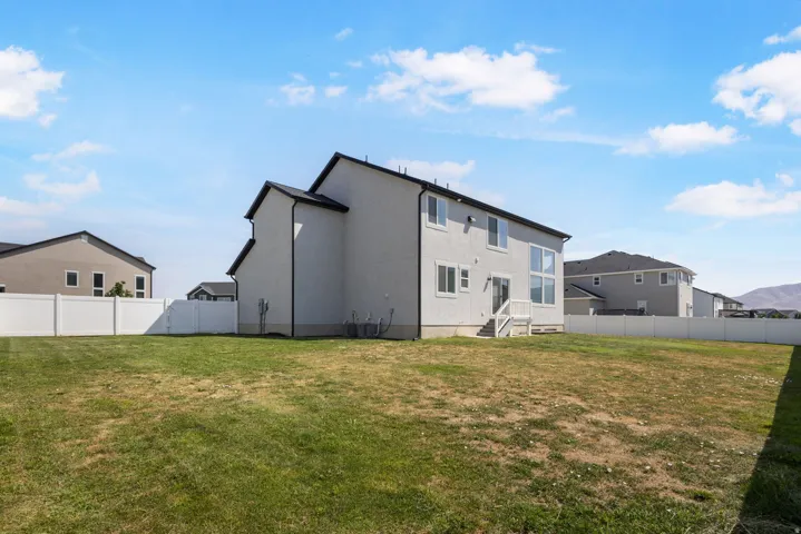 Expansive backyard featuring a stucco exterior, white vinyl fencing, and a multi-pane window design