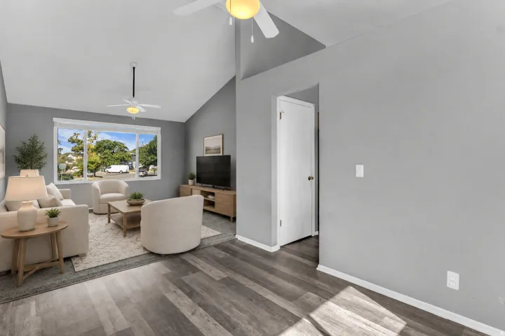 Vaulted ceiling, ceiling fan, large windows, wood-finish flooring, and a white interior door