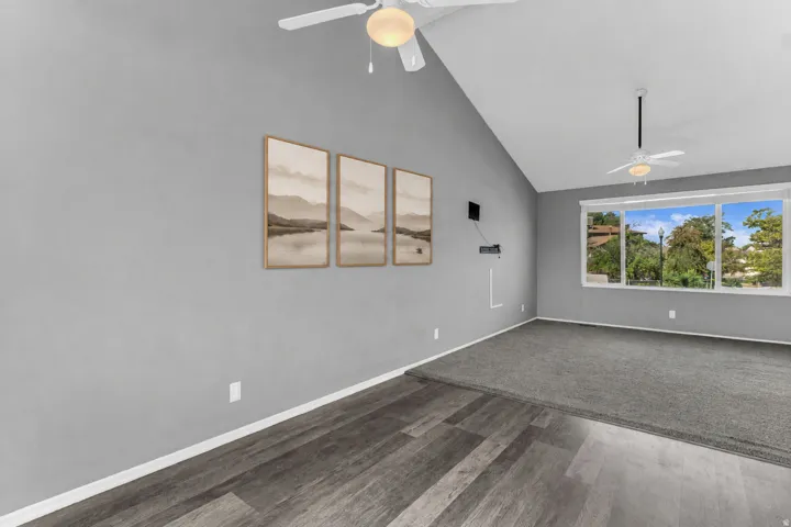 Vaulted ceiling, two ceiling fans, large window, wood-finish flooring, and carpeted area