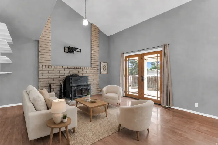 Vaulted ceiling, brick fireplace with wood stove, wood-finish flooring, and double patio doors