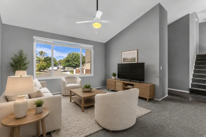 Expansive living area with vaulted ceilings, a large picture window, and wood-finish media console