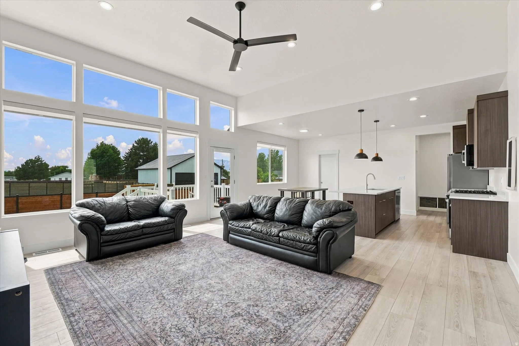Open-concept living area with extensive windows, light wood-finish flooring, and recessed lighting. NATURAL LIGHT