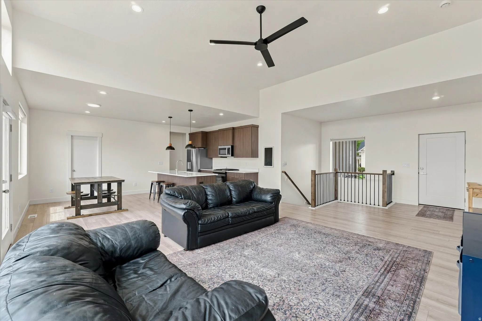 Vaulted ceilings with recessed lighting, light wood-finish flooring, and a kitchen with an island featuring pendant lighting and a stainless steel refrigerator