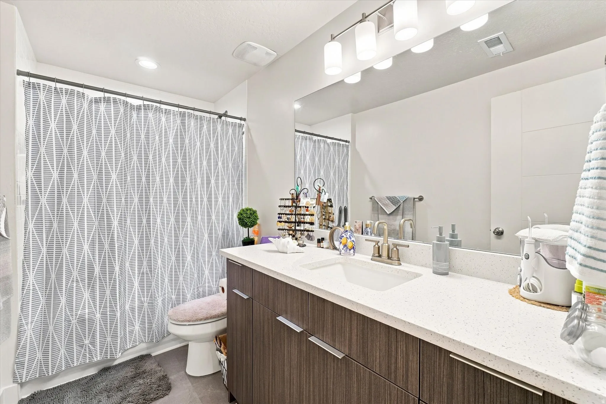 Bathroom vanity with a white countertop and integrated sink, modern wood-finish cabinetry, and a large wall-mounted mirror