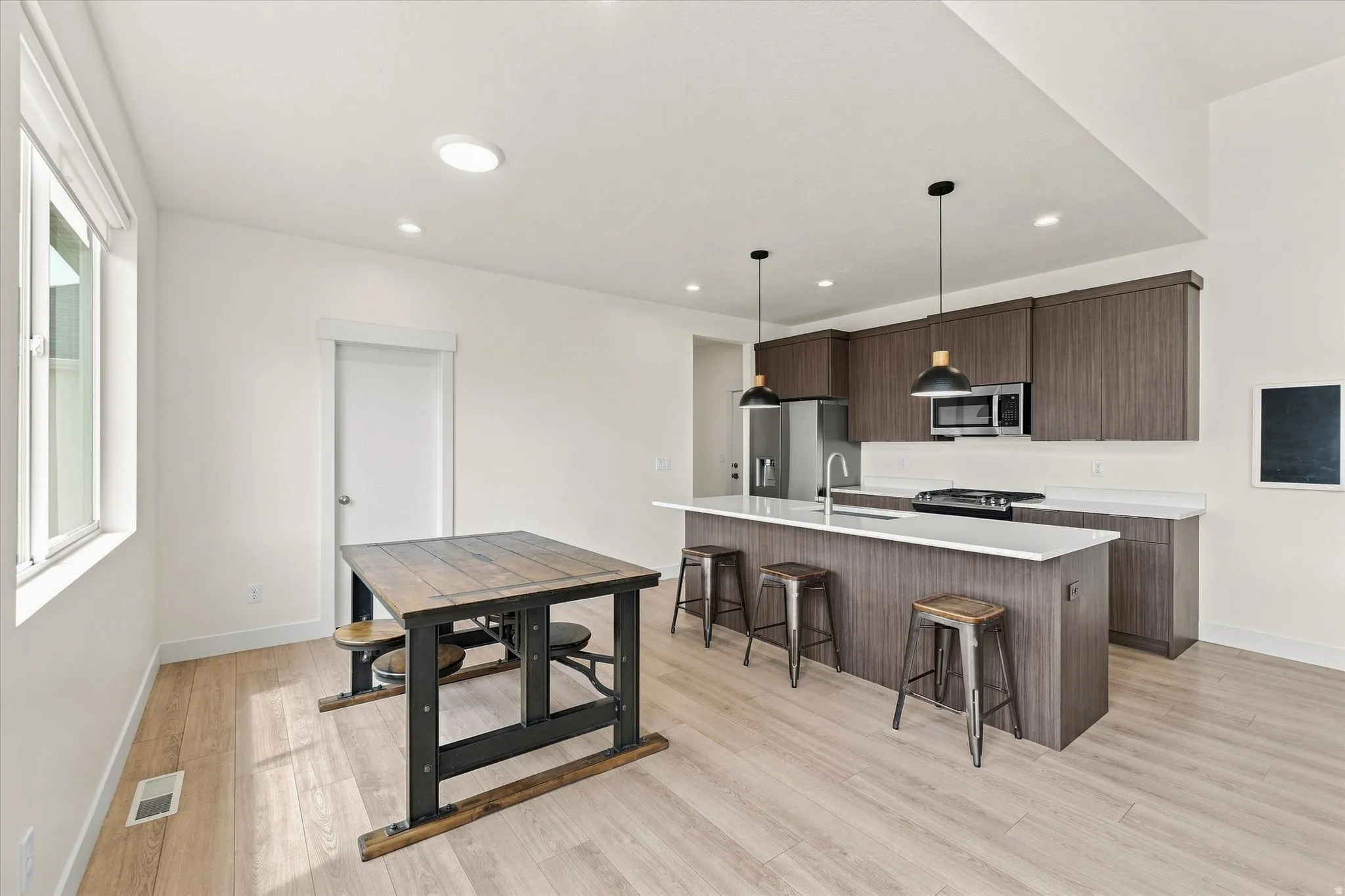 Kitchen featuring wood-finish cabinetry, stainless steel appliances, a center island with counter seating, and light wood-finish flooring