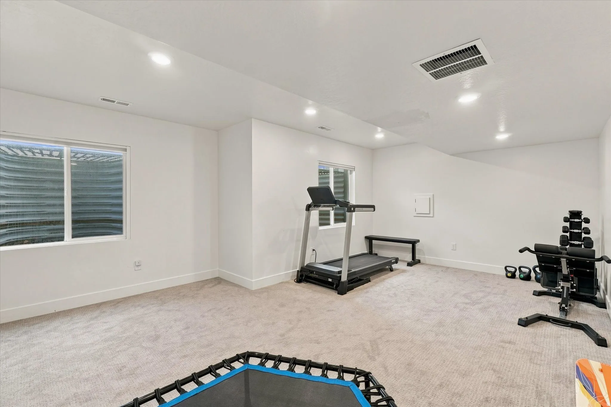 Recessed lighting illuminates a spacious room featuring light-toned carpet flooring and white walls