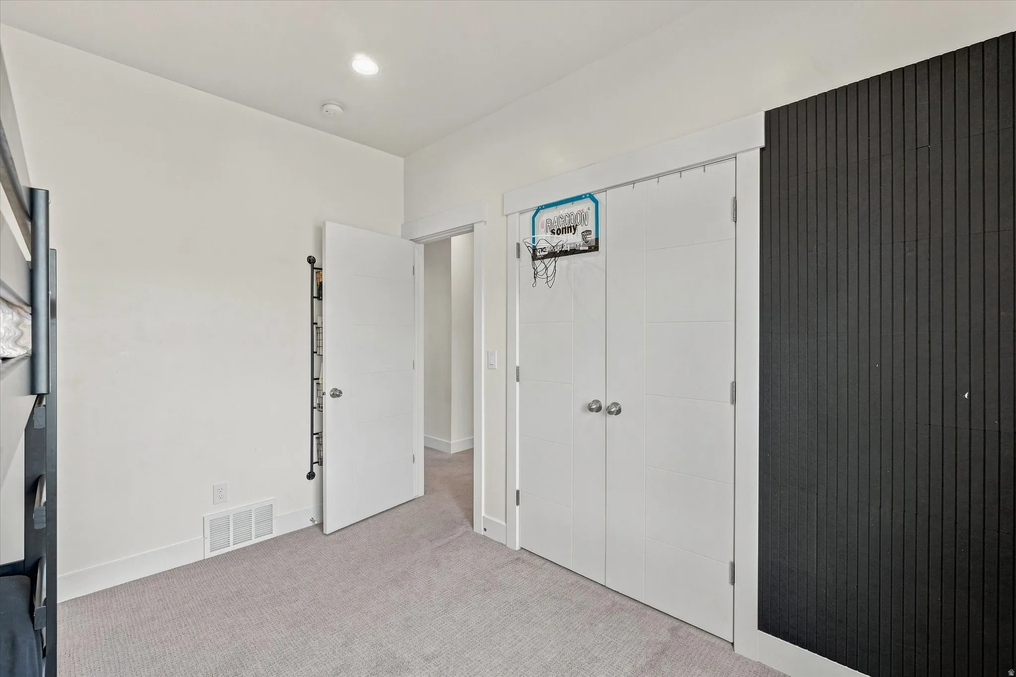 Plush carpet flooring, recessed ceiling lighting, a dark accent wall with vertical paneling, and white bi-fold closet doors