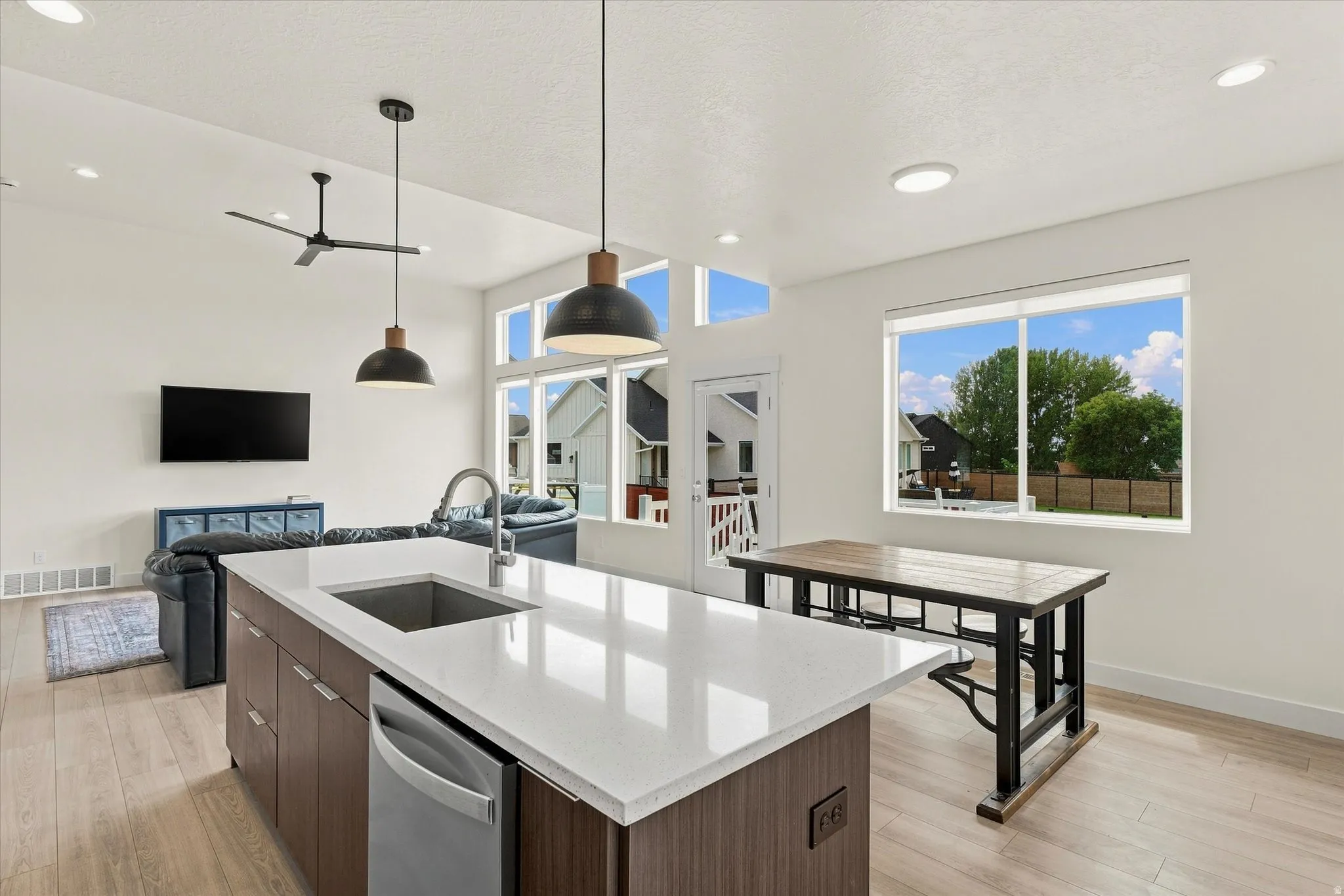 Open-concept living space featuring wood-finish flooring, a kitchen island with a single-basin sink, stainless steel dishwasher, and quartz-finish countertop